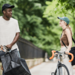 Two cyclists chatting by their bikes on a tree-lined street