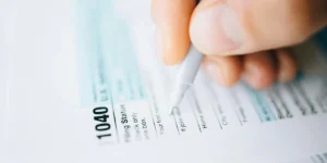 A person filling out a U.S. 1040 tax form with a pen, representing tax-related considerations for DUI expenses