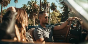Man driving a vintage convertible with a woman passenger on a sunny day in California, palm trees lining the street