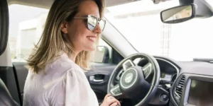 Smiling woman wearing sunglasses sitting in the driver's seat of a car, ready to drive again after reinstating her license