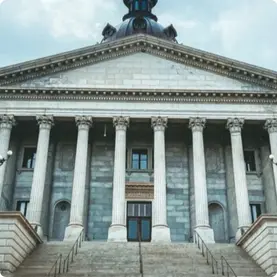 Front view of a government building with stone steps and large columns under a cloudy sky