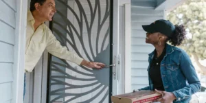 Smiling food delivery driver handing pizza boxes to a customer at their front door