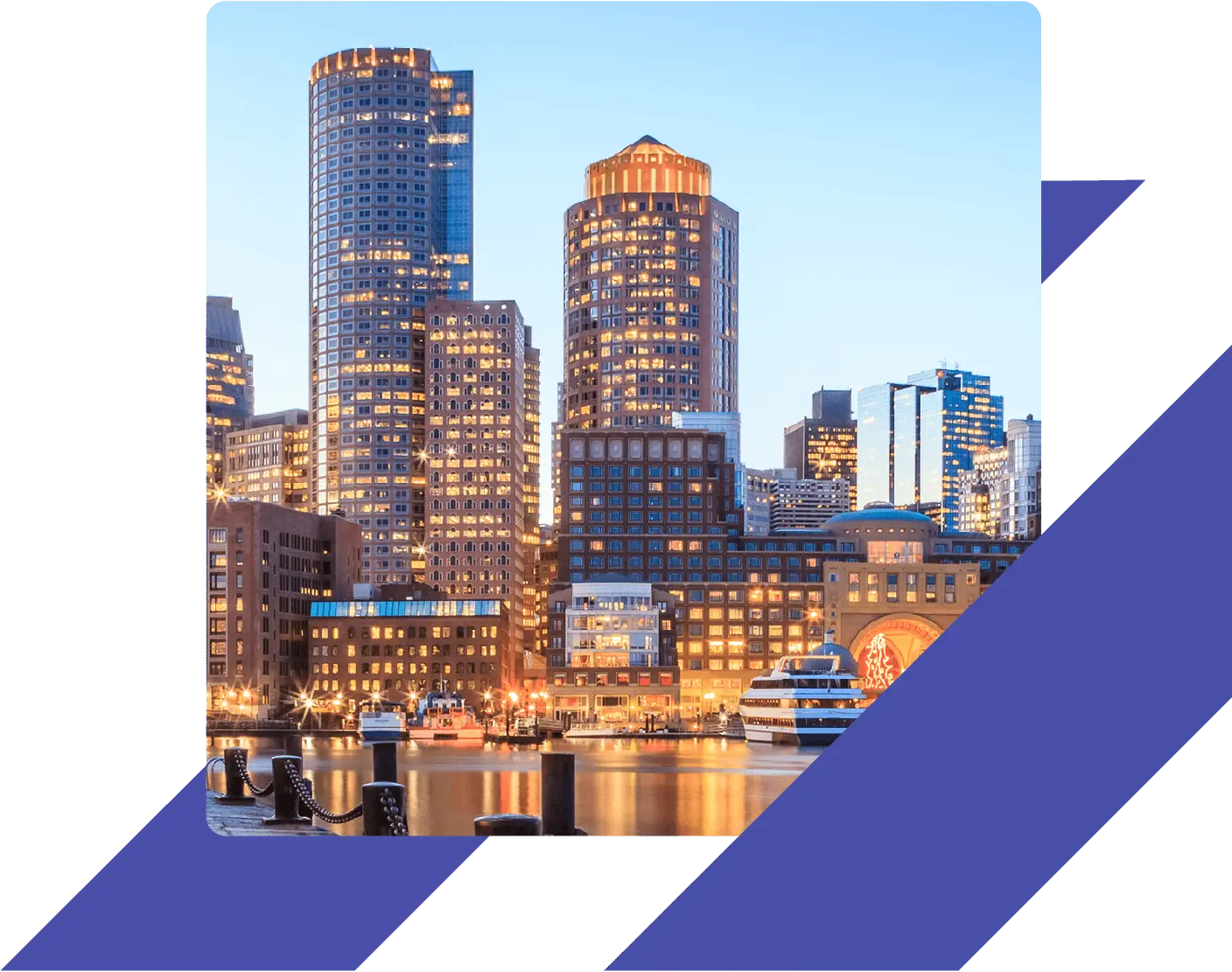 Boston Harbor at dusk with boats docked along the waterfront and the city skyline lit up in the background.