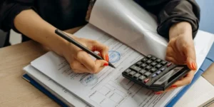 Person reviewing financial documents and writing notes while holding a calculator