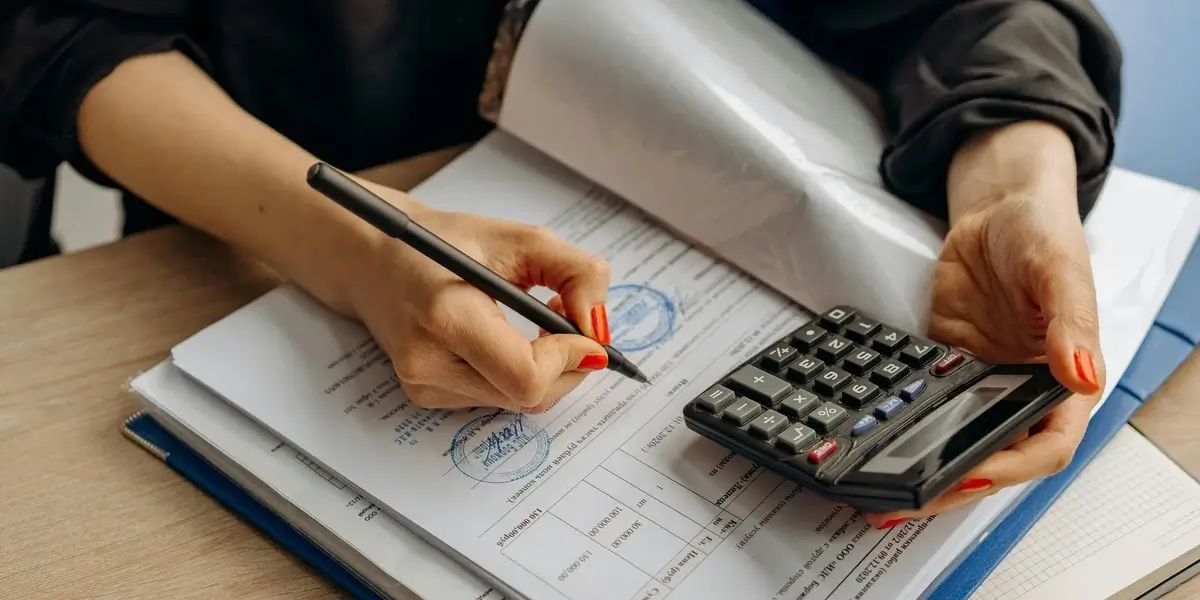 Person reviewing financial documents and writing notes while holding a calculator