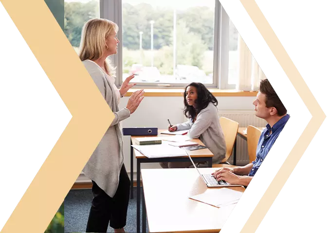 A teacher standing at the front of a classroom, actively speaking to a room full of attentive students.
