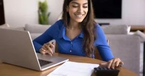 A woman smiling and typing on a calculator.