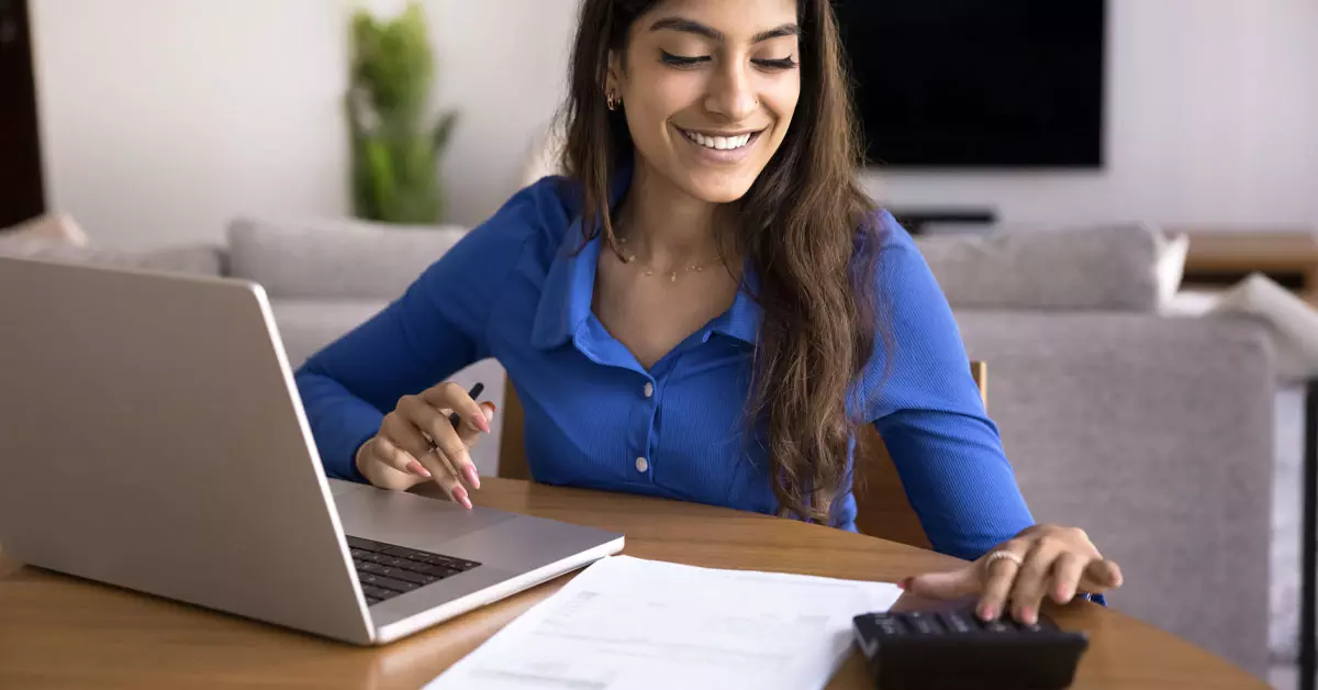A woman smiling and typing on a calculator.