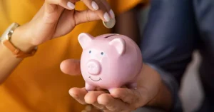 A picture of a hand inserting a coin into a piggy bank.