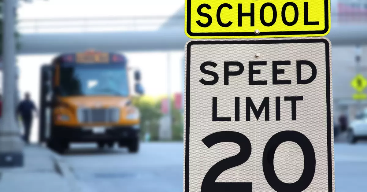 A closeup picture of a school sone speed limit sign, with a school bus in the background.