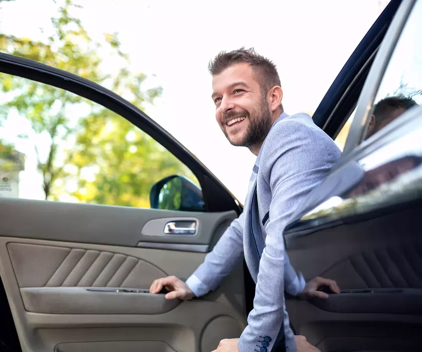 Man smiling and sitting on the edge of his car's driver's seat with the door open.