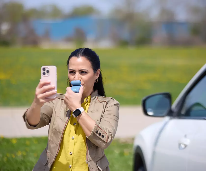 Woman using a Keepr breathalyzer outside of her car.